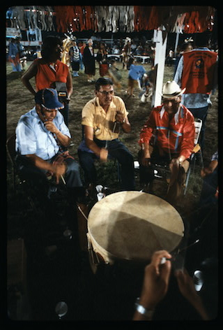 People sit in a circle around someone playing a drum